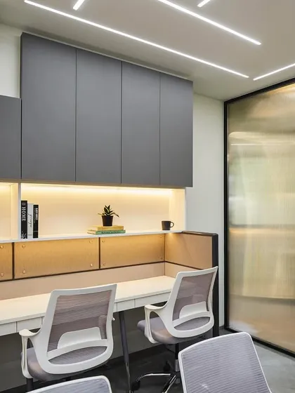 A closer look at the workstation design. Fluted glass partitions offer a sense of personal space without closing off the area, complemented by ample overhead storage in a sleek grey finish to maintain a clutter-free environment.