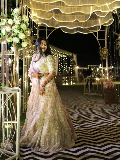 The bride posing against the beautifully lit decor of her Sangeet night, showcasing her outfit and the event's ambiance.