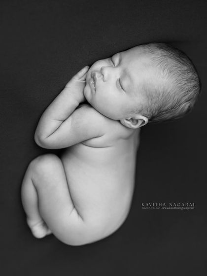 A classic newborn pose, curled up on their side in black and white. This style emphasizes the baby's tiny, perfect form and the quiet stillness of their sleep.