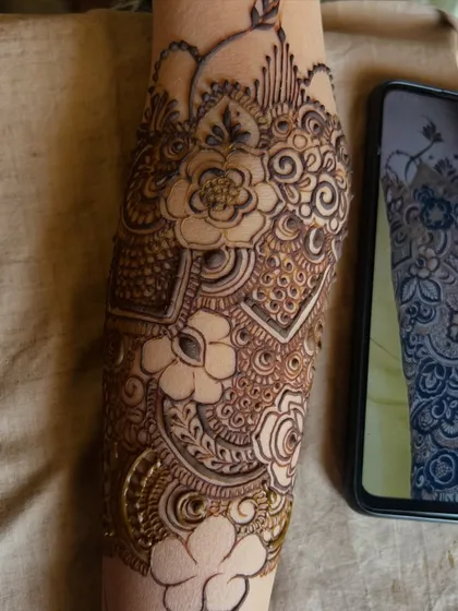 A work-in-progress shot of Bride Rumana's mehendi, showing the reference photo on the phone and the design coming to life.