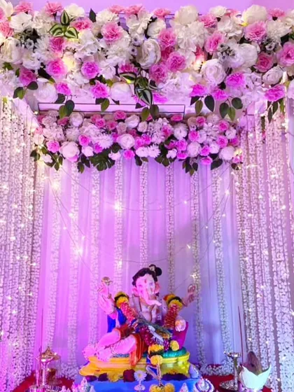 This setup features a canopy of pink and white flowers with curtains of hanging floral strings and fairy lights. The purple lighting gives the entire mandap a magical glow.