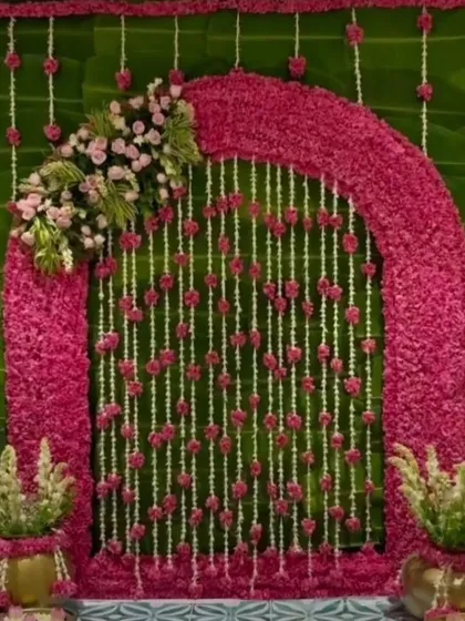 For this Ganpati celebration, I designed a vibrant floral arch using pink blossoms against a lush green backdrop of banana leaves. The hanging strings of jasmine and roses add a delicate, traditional touch.