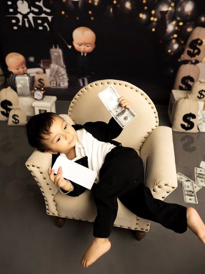 Lounging like a true boss, this little guy is enjoying his themed first birthday session. The setup includes a miniature armchair and a backdrop that completes the executive look.
