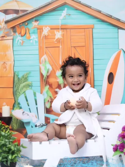 A cheerful beach-themed photoshoot, complete with a beach hut backdrop, surfboards, and a happy baby enjoying the scene.
