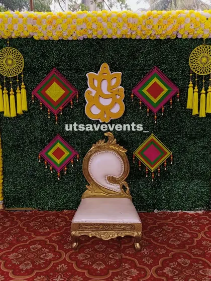 A colorful Mehendi backdrop with a greenery wall, a Ganesha cutout, and vibrant dreamcatcher-style hangings. The single golden chair is perfect for the bride-to-be.