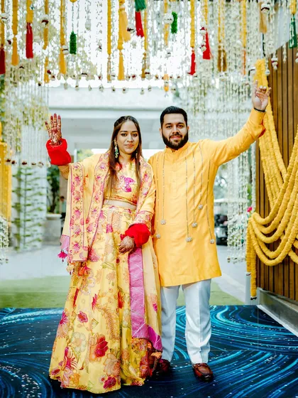 The couple makes a grand entrance at their Haldi ceremony, waving to guests under a beautiful floral decor.
