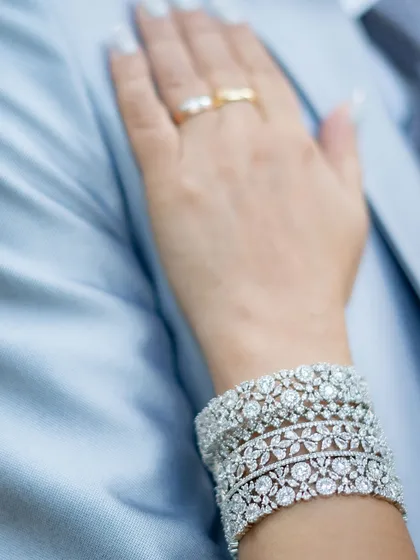 A close-up detail shot of the wife's hand, adorned with beautiful diamond bracelets and her wedding ring, resting on her husband's suit.