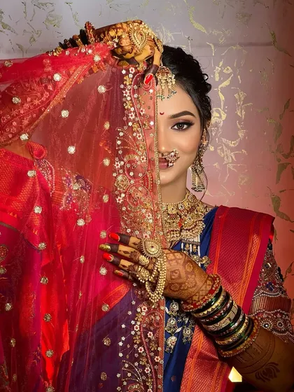 A coy bride peeks from behind her red veil, showing off her dramatic eye makeup.