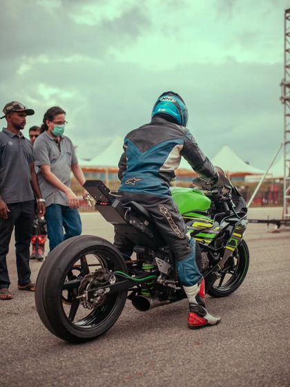 A rider on a green Kawasaki with an extended swingarm gets ready to race, with crew members offering support.