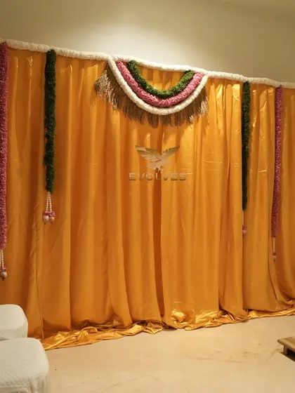 A simple and traditional pooja backdrop for a house warming, using a bright yellow fabric and classic floral thorans.