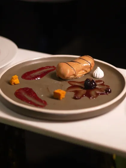 An elegant eclair presented on a rustic plate, with artistic smears of berry coulis and meringue kisses. This is dessert with flair.
