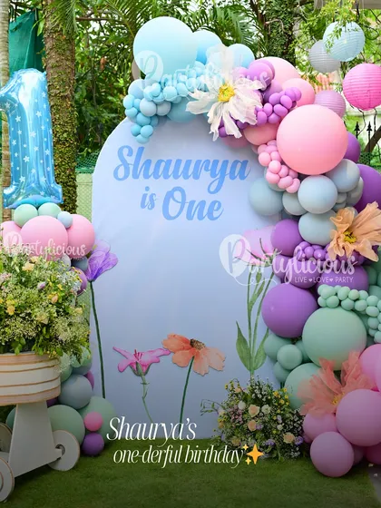 Shaurya's 'one-derful' first birthday. This beautiful outdoor setup features a soft, pastel balloon garland accented with flowers, set against a custom-painted backdrop. It’s a dreamy and gentle theme for a first milestone.