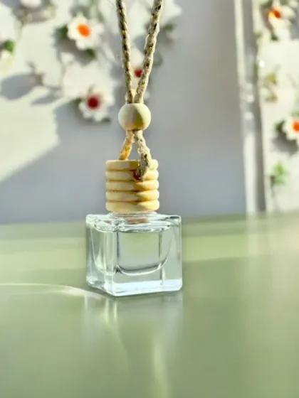 A clean product shot of the hanging car freshener. The simple design, featuring a glass bottle and a wooden diffuser cap, is both functional and aesthetically pleasing.