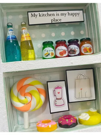 "My kitchen is my happy place." A close-up of the miniature pantry shelf in the baker's frame, stocked with tiny jam jars and drinks.