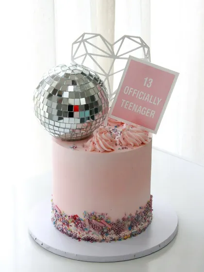 Officially a teenager! This cake brings all the glam with a disco ball topper, sprinkles, and a fun, modern design for a 13th birthday.