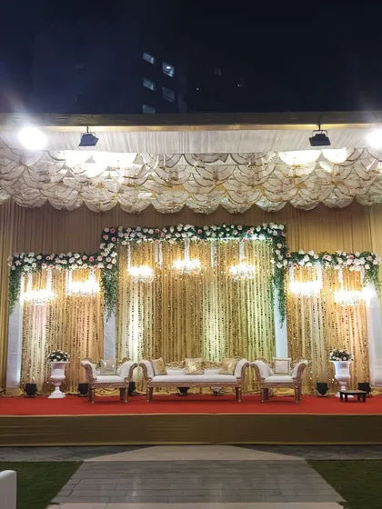 A grand, traditional reception stage with gold and white decor, featuring elegant sofas and chandeliers.
