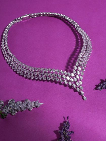 A stunning diamond necklace laid out on a rich purple satin fabric, accented with sprigs of lavender. The color and texture combination screams luxury and sophistication.