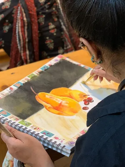 A student paints a still life of yellow peppers, mastering the art of capturing light and texture with watercolors.