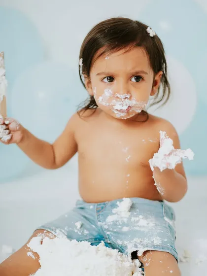 He's got his spoon and a handful of cake, ready for anything. This photo shows the playful energy of a one-year-old boy.