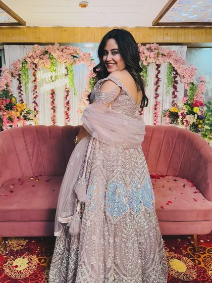 A happy client posing in a beautiful pastel purple lehenga with blue accents. This is a perfect outfit for a wedding guest, offering a unique color combination and elegant design.