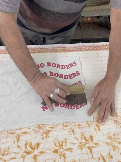 An artisan printing the 'No Borders' logo on a tote bag. This was for a special workshop focused on community and collaboration.