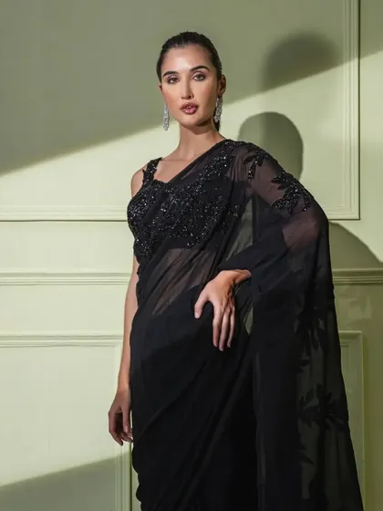 A portrait shot highlighting the delicate floral embroidery on the shoulder and blouse of the timeless black georgette saree.