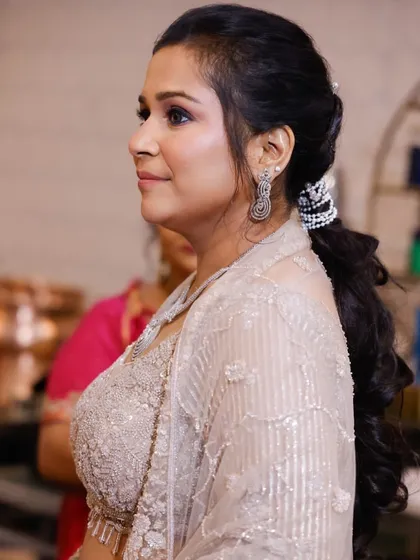 A side profile of a client with a beautiful party hairstyle. The soft, curled ponytail is adorned with pearl accessories for an extra touch of elegance.