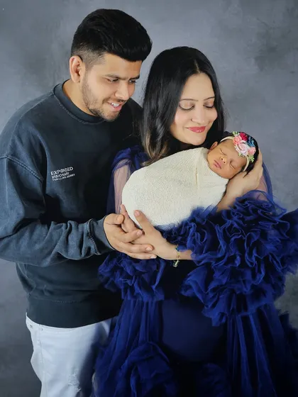 A classic portrait of new parents adoring their sleeping newborn. The mother is wearing a beautiful blue ruffled gown, adding a touch of elegance to this family's first photoshoot.