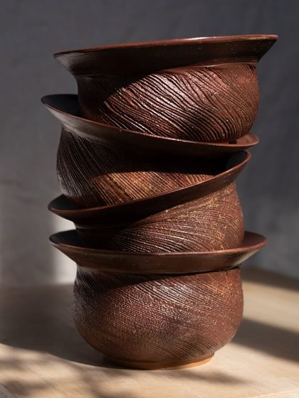 A stack of beautifully textured planters from Aastha's 'Dhora' collection, their surfaces evoking the windswept patterns of sand.