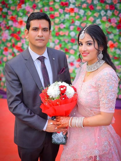 A formal portrait of the couple with a bouquet against a flower wall.