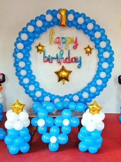 A first birthday setup with a Minnie Mouse theme, featuring a circular balloon frame and character pillars in blue and white.