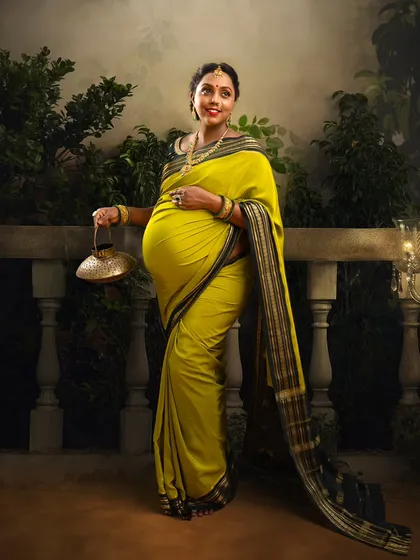 Posed with elegance, this mother-to-be holds a traditional purse, her yellow saree glowing against a misty, atmospheric backdrop. A timeless and graceful maternity portrait.