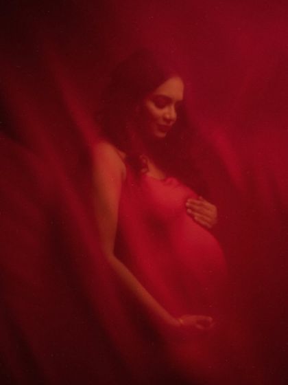 A quiet moment in red. This image captures the mother's gentle expression as she cradles her bump, enveloped in a soft, crimson glow.