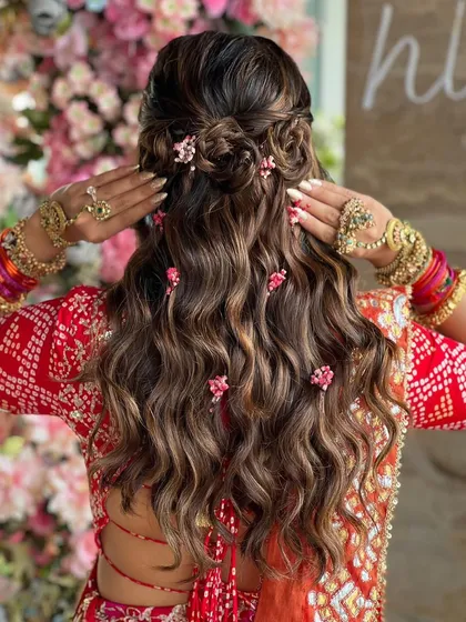 A closer look at this floral and curly hairstyle. The way the small flowers are tucked into the braids and curls gives it a very whimsical and romantic feel, perfect for a garden Mehendi.