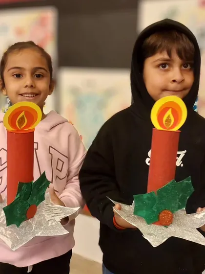 The joy of the season shines through as these two young artists show off their completed Christmas candle holders, complete with paper flames and holly leaves.