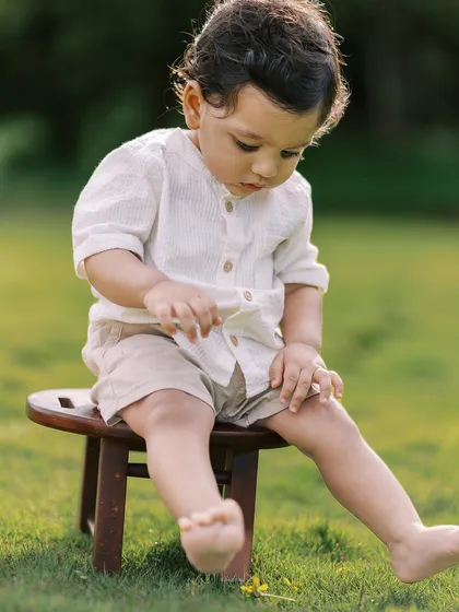 A different angle from the same lakeside shoot, showing the baby's thoughtful expression as he sits on a stool.