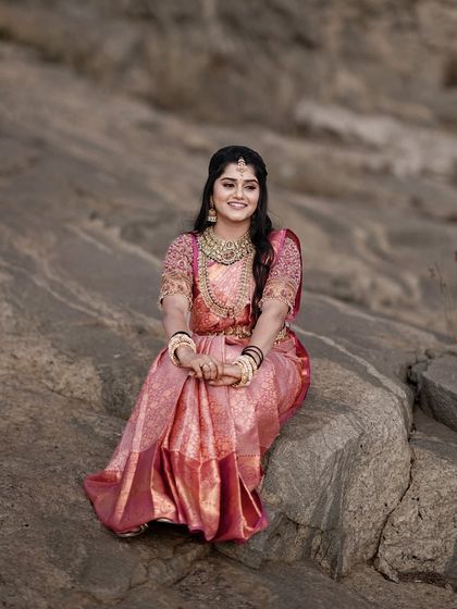 A beautiful bridal portrait of the bride seated on a rock. Her joyful smile and stunning pink saree stand out against the natural, rugged background.