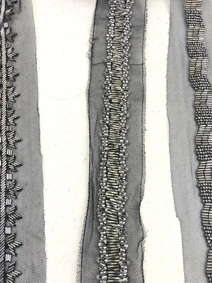 A trio of hand-beaded trims on a net base. Each lace features a unique pattern using metallic bugle beads, showcasing the variety of modern, linear designs available for couture embellishment.