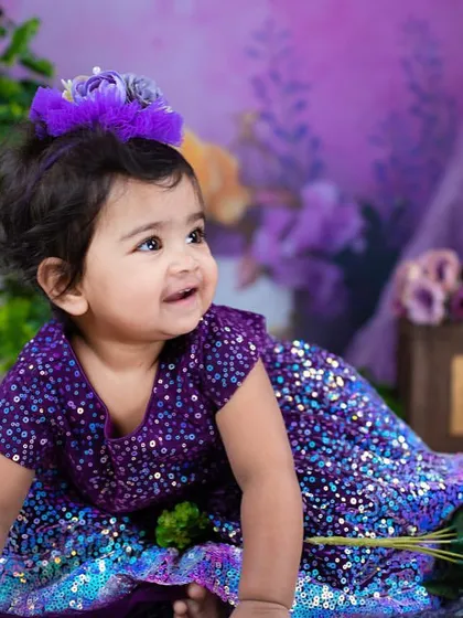 A little girl in a sparkling purple dress, celebrating her first birthday. This combines a traditional dress style with a modern, glittery fabric.