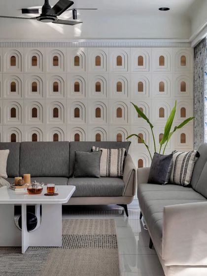 The grey sofa and neutral textiles provide a calm counterpoint to the intricate, custom-designed feature wall.