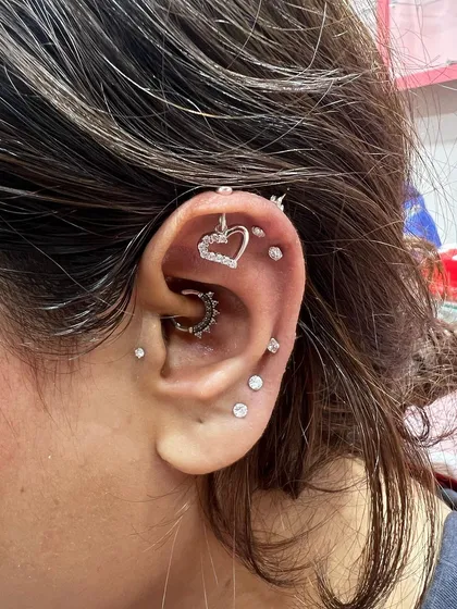 A fully loaded ear stack featuring a heart-shaped hanging, a daith hoop, and a constellation of solitaire studs running up the ear.