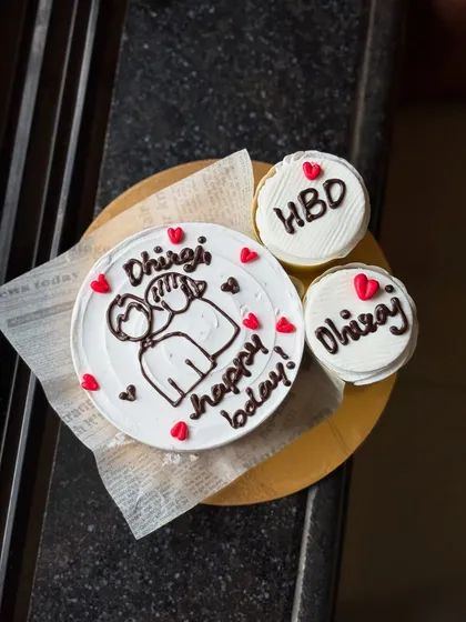 This is another view of the personalized birthday set for Dhiraj, showing the bento cake and cupcakes on a wooden board. The hand-drawn style gives it a really personal feel.