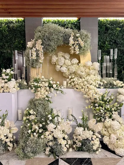 A stunning dessert table backdrop, featuring a wall of cascading white flowers against a green hedge wall.