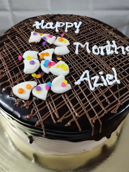 A chocolate cake celebrating Aziel's 3-month milestone, topped with a chocolate drizzle and colorful candies.
