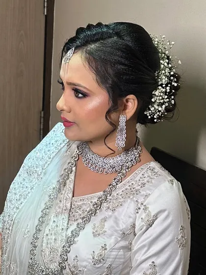 A side profile of my client for her reception. The elegant braided bun is adorned with baby's breath, and her makeup is a sophisticated look with smoky eyes, paired with a stunning diamond necklace.