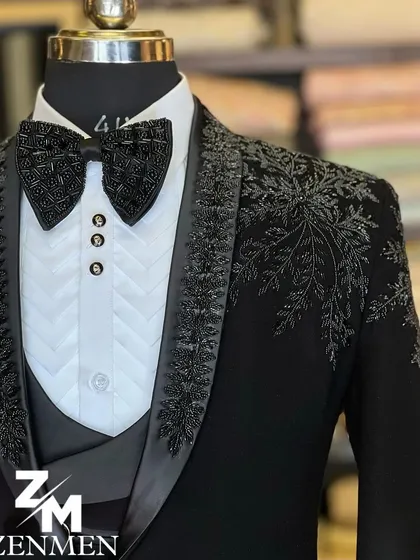 A close-up of a black tuxedo with black floral and leaf embroidery on the lapel and shoulder. The matching embellished bow tie completes this elegant ensemble.