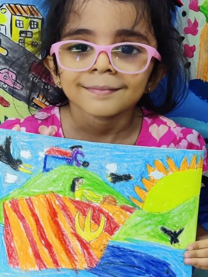 A young girl with pink glasses proudly shows her imaginative landscape. Her drawing features rolling hills with colourful stripes, a bright sun, and birds flying in the sky, a true expression of her inner world.