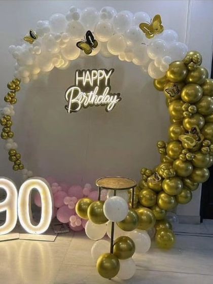 Celebrating a 90th birthday in style with this gold and white balloon arch. The setup includes large light-up numbers and butterfly accents for a graceful touch.