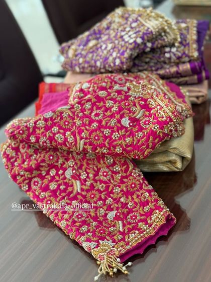 A stack of heavily embroidered bridal blouses in pink and purple.