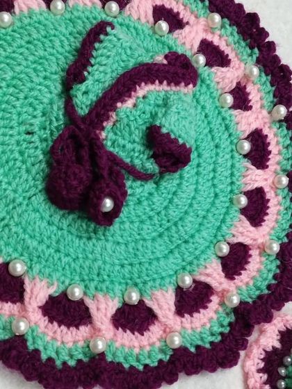 This woolen dress combines mint green, pink, and purple, and is studded with pearls. It comes with a matching cap to complete the cozy winter outfit.